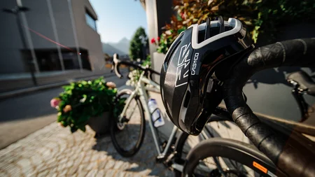 Fietshelm op racefiets stuur bij bloemen en stedelijke achtergrond met bergen