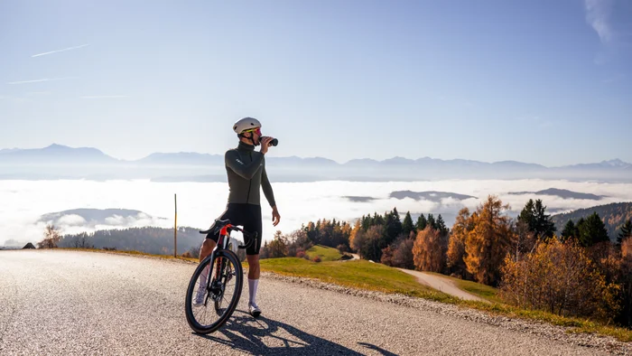 Cyclist drinking water on mountain road with fog and mountains in background