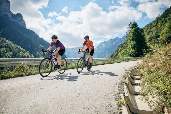 Twee fietsers op bergweg bij zonnig weer met blauwe lucht en wolken