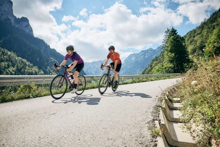 Twee fietsers op bergweg bij zonnig weer met blauwe lucht en wolken