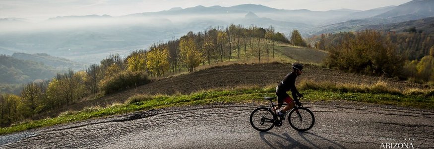 Radfahrer fährt auf Bergstraße mit Nebel und Hügeln im Hintergrund