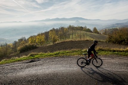 Cyclist riding on mountain road with mist and hills in background