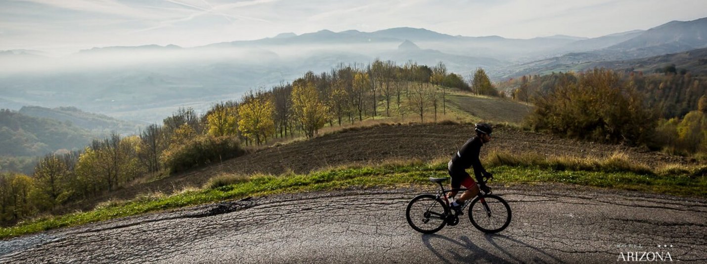 Radfahrer fährt auf Bergstraße mit Nebel und Hügeln im Hintergrund