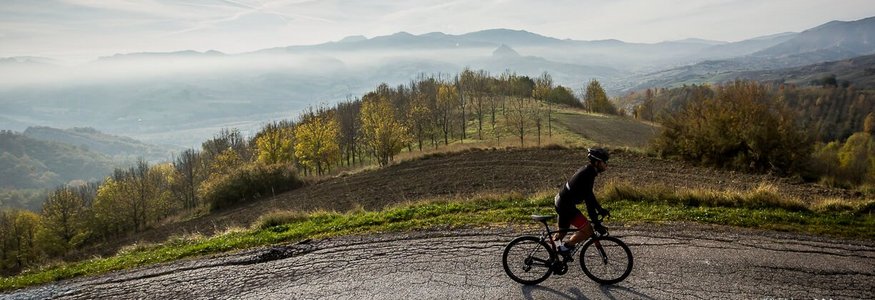Ciclista che pedala su strada di montagna con nebbia e colline sullo sfondo