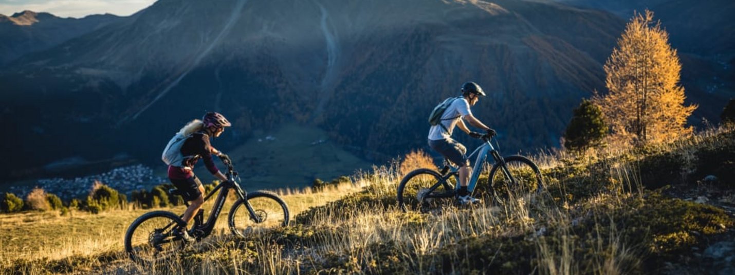 Twee mountainbikers fietsen heuvelopwaarts met bergen op de achtergrond