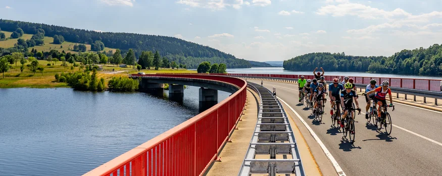 Gruppe von Radfahrern auf einer Brücke über einen Fluss bei sonnigem Himmel