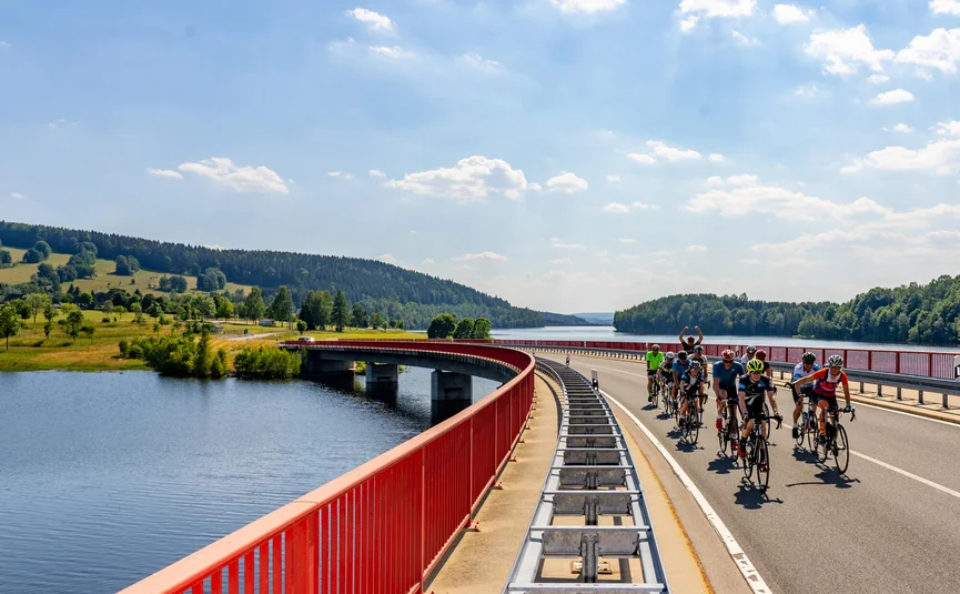 Gruppe von Radfahrern auf einer Brücke über einen Fluss bei sonnigem Himmel