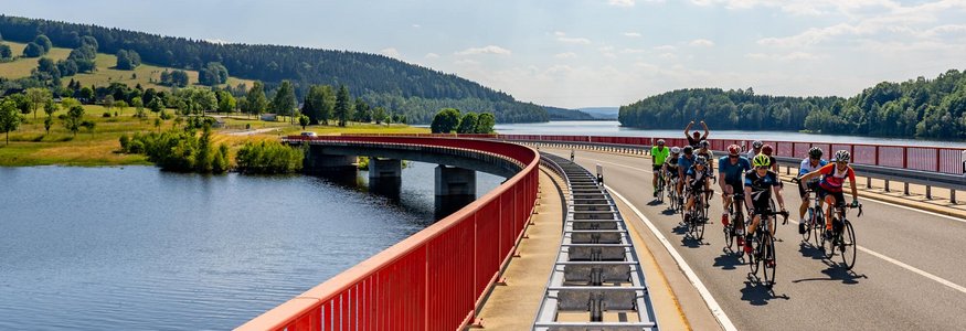 Gruppe von Radfahrern auf einer Brücke über einen Fluss bei sonnigem Himmel