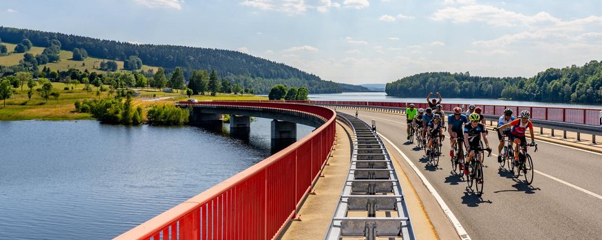 Gruppe von Radfahrern auf einer Brücke über einen Fluss bei sonnigem Himmel