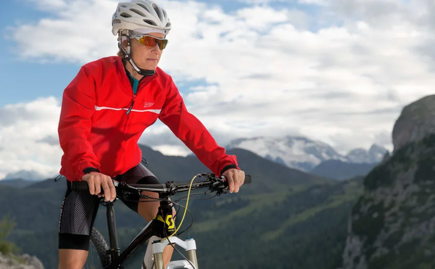 E-Bike Experience - 4 nights Vrouw in rode jas mountainbiken in bergachtig landschap