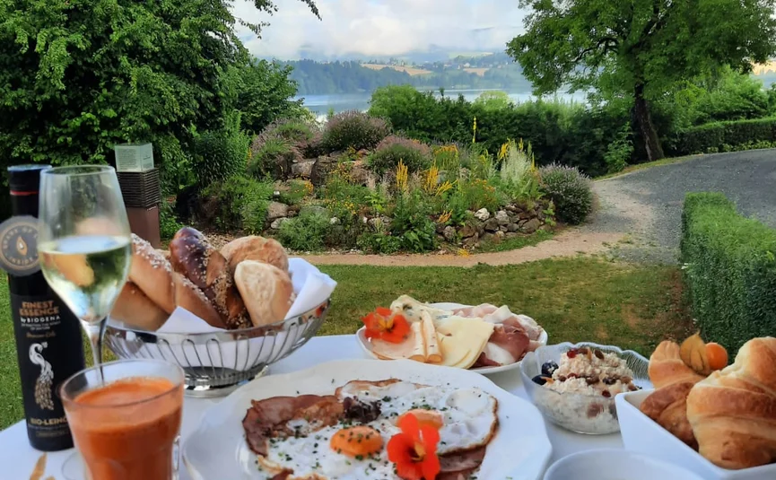Frühstückstisch draußen mit Eiern, Brötchen, Kaffee und Blick auf Garten und See