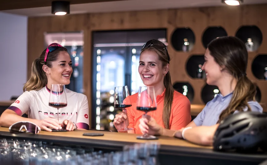 Drei Frauen in Sportkleidung trinken Rotwein an einer Bar