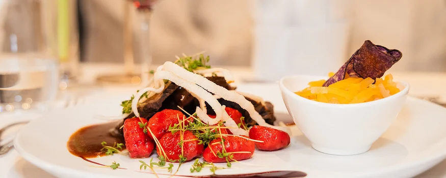 Elegantes Gericht mit roter Sauce, Gemüse und Rotwein im Hintergrund