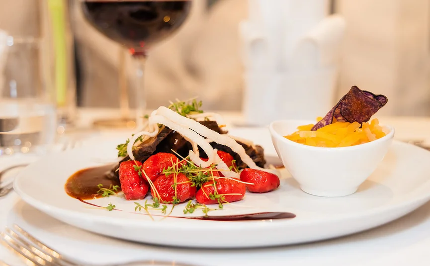 Elegantes Gericht mit roter Sauce, Gemüse und Rotwein im Hintergrund