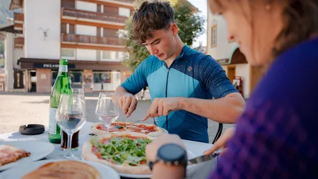 Jonge man snijdt pizza aan tafeltje buiten