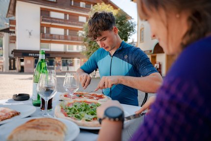 Junger Mann schneidet Pizza an einem Tisch im Freien