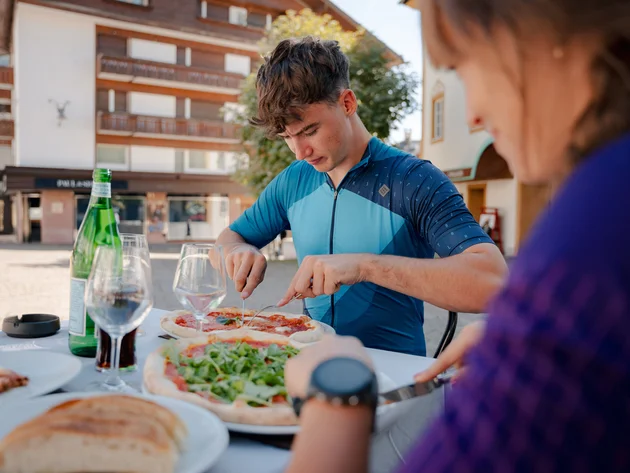 Jonge man snijdt pizza aan tafeltje buiten