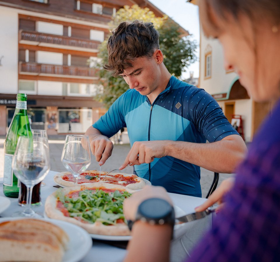 Junger Mann schneidet Pizza an einem Tisch im Freien