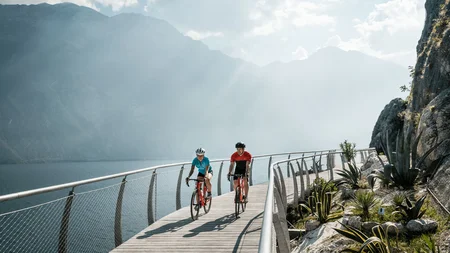 Twee fietsers op een steiger bij het meer met bergen op de achtergrond