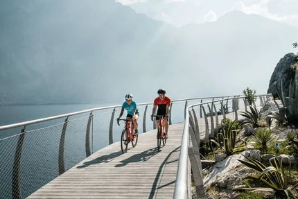 Twee fietsers op een steiger bij het meer met bergen op de achtergrond
