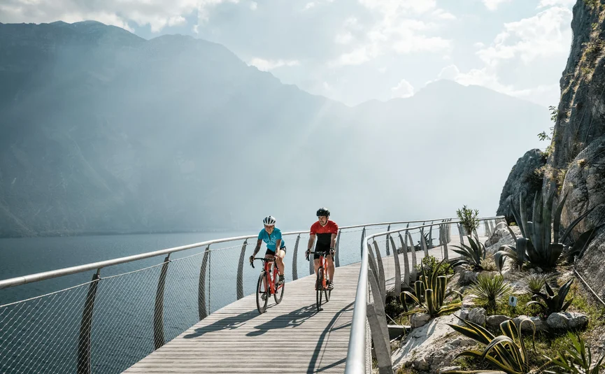 Due ciclisti su una passerella vicino al lago con montagne sullo sfondo