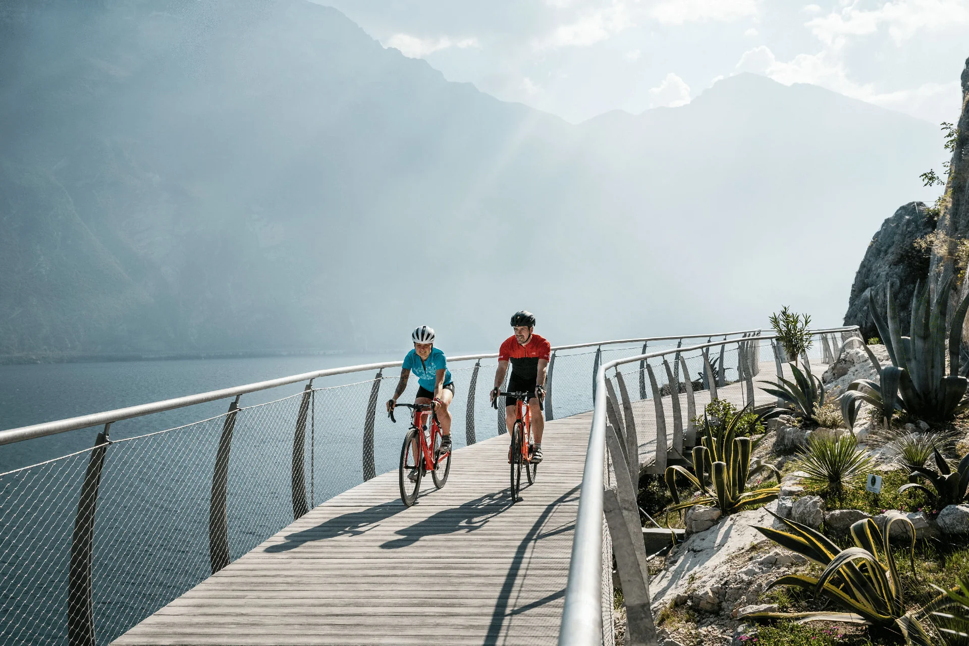 Roadbike Holidays © Alex Moling Zwei Radfahrer auf einem Steg am See mit Bergen im Hintergrund