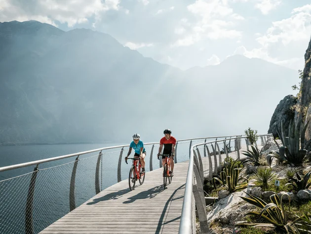 Twee fietsers op een steiger bij het meer met bergen op de achtergrond