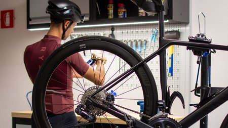 Person mit Helm repariert Rennrad in Werkstatt mit Werkzeug