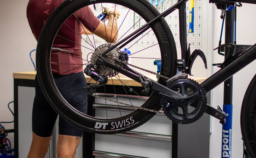 Person wearing helmet repairing road bike in workshop with tools