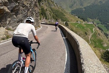 Zwei Radfahrer fahren eine Bergstraße mit Felswand und Panoramablick hinauf