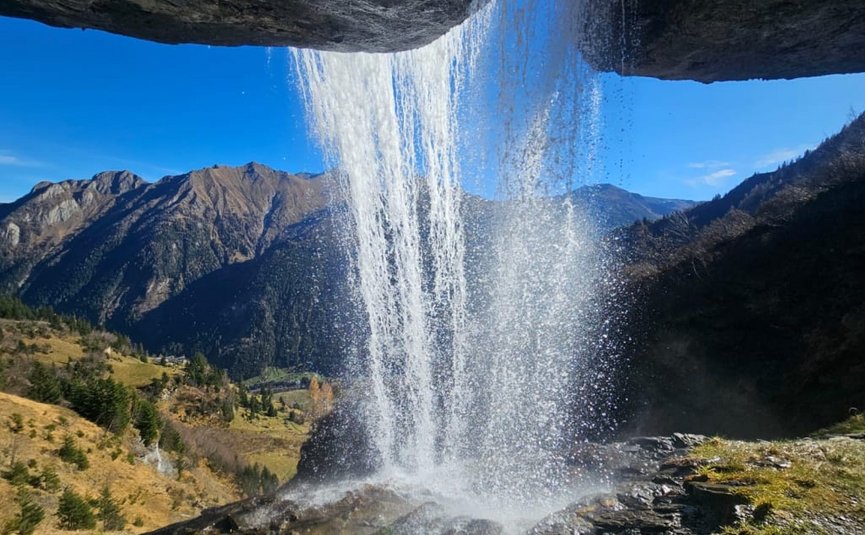Wasserfall fällt hinter Felsvorsprung in bergiger Landschaft bei klarem Himmel