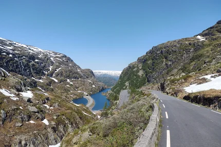 Mountain road beside lake and snow-capped mountains under clear blue sky