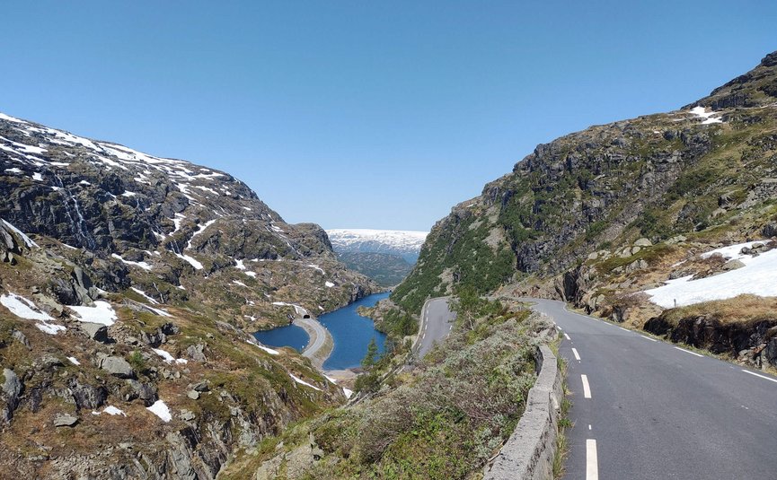 Strada di montagna accanto a lago e montagne innevate sotto cielo azzurro