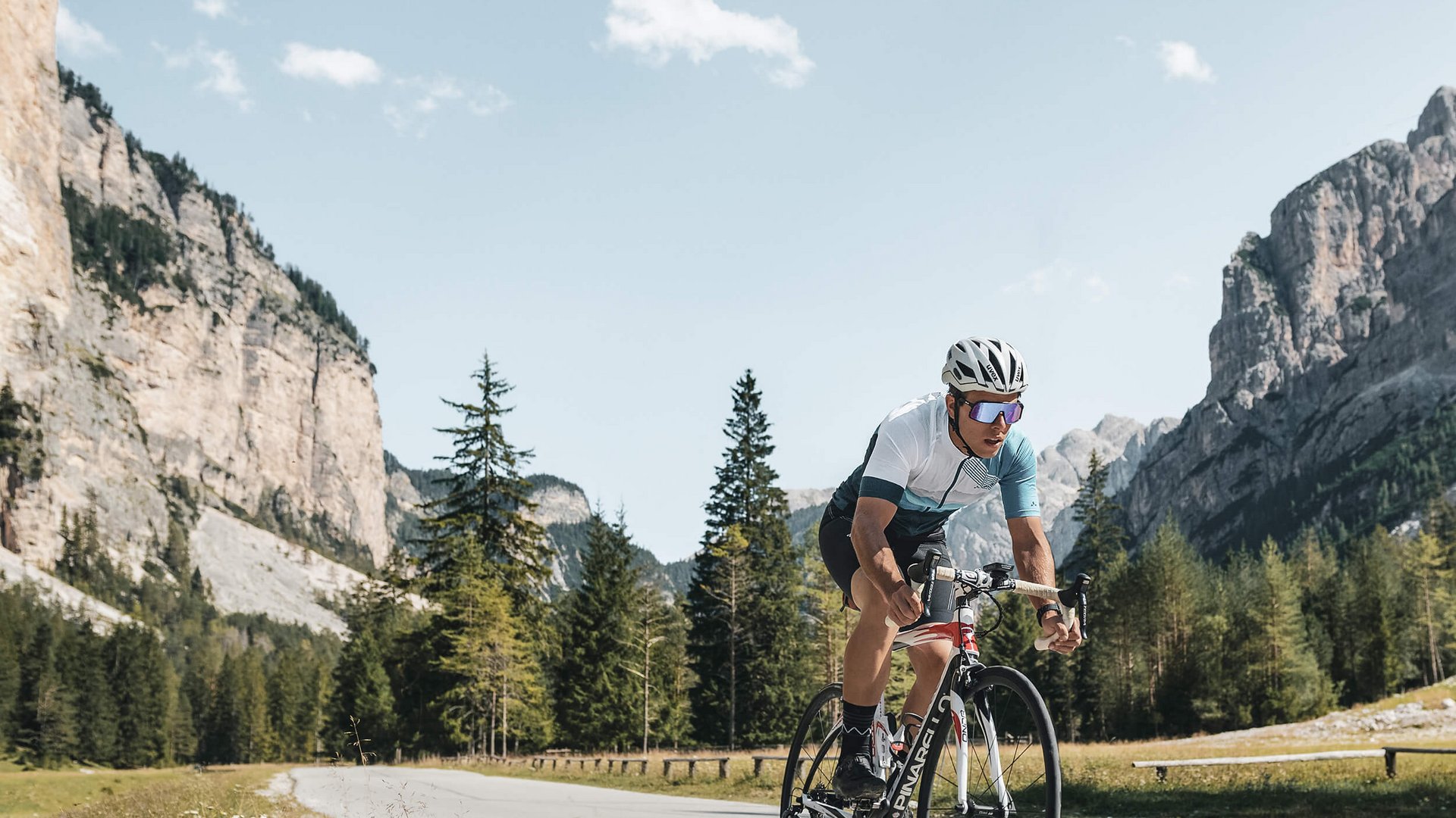 Fahrradfahrer fährt auf Bergstraße mit Felsen und Bäumen im Hintergrund