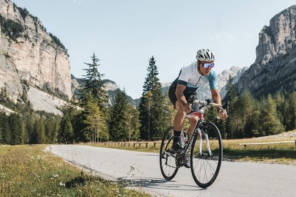 Fietser rijdt op bergweg met kliffen en bomen op de achtergrond