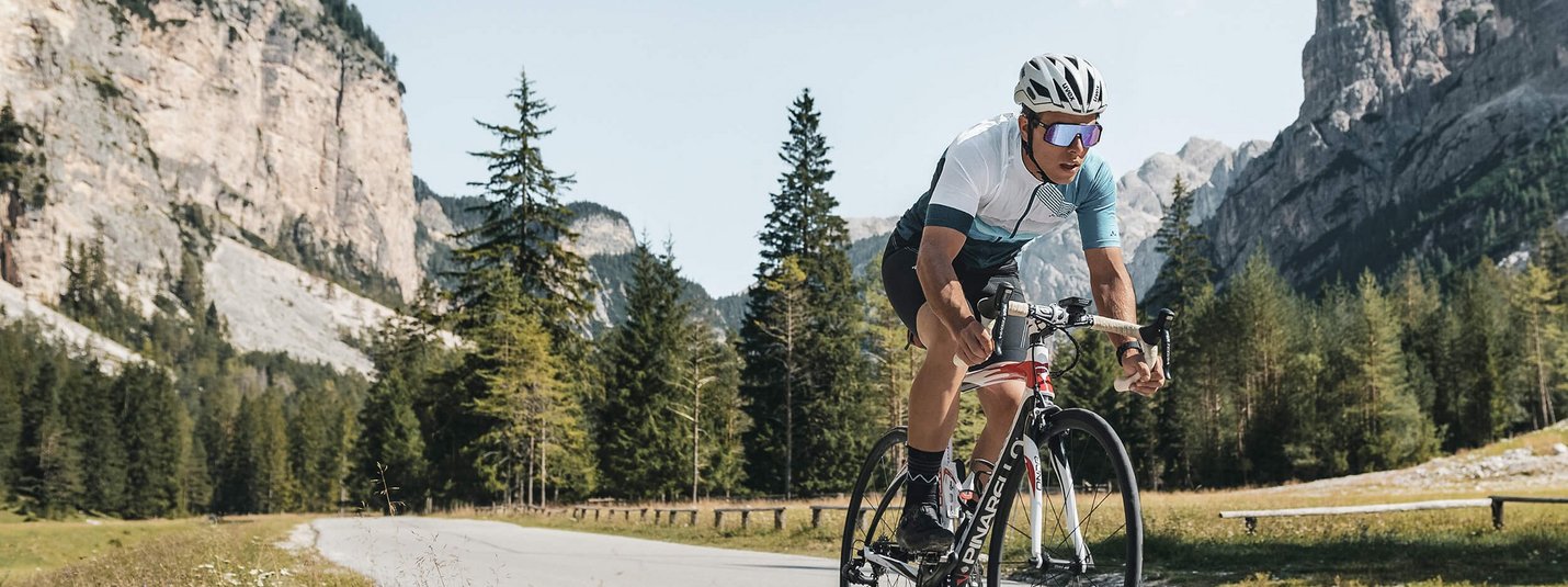 Ciclista su strada di montagna con scogliere e alberi sullo sfondo
