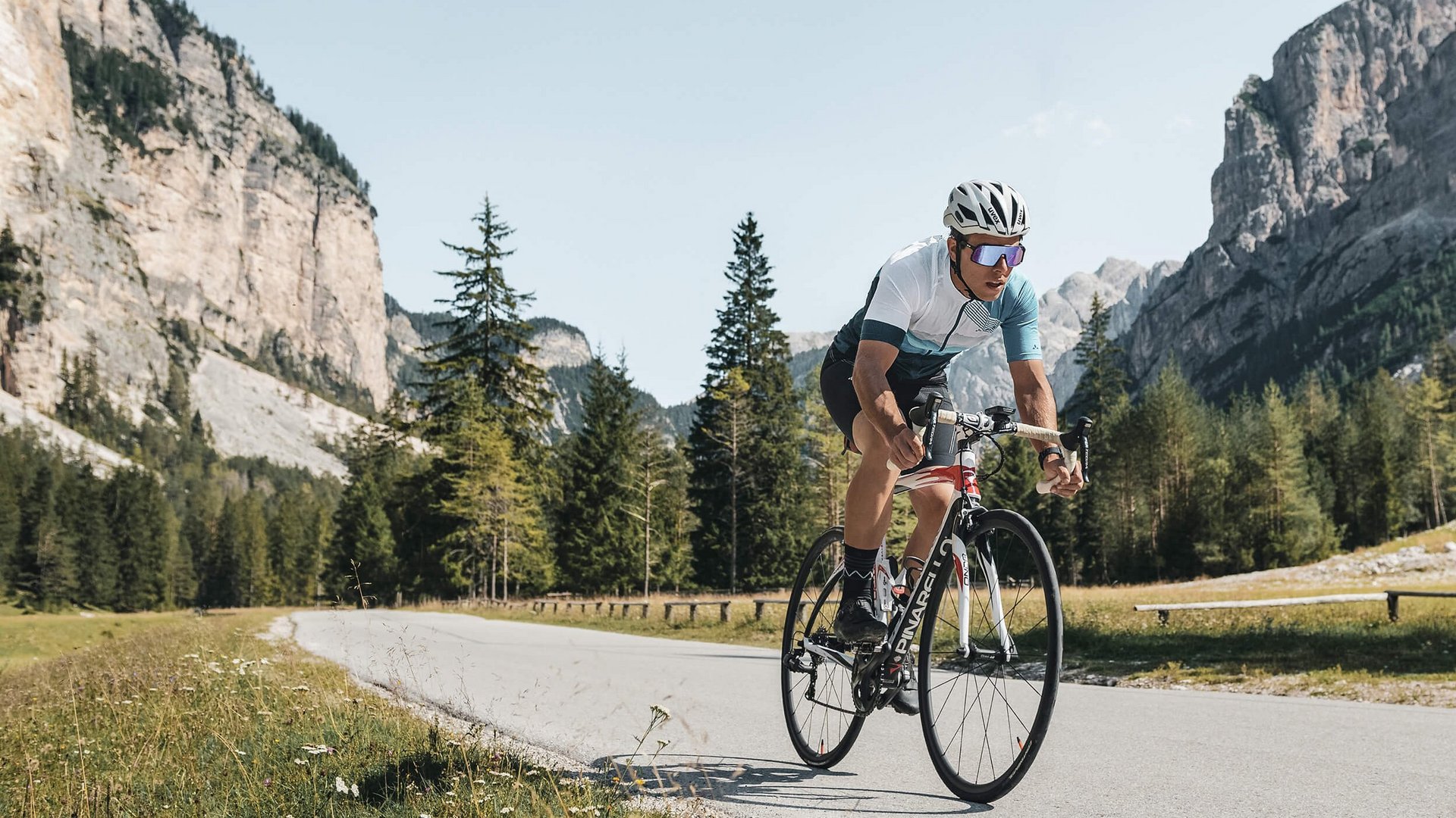 Fahrradfahrer fährt auf Bergstraße mit Felsen und Bäumen im Hintergrund