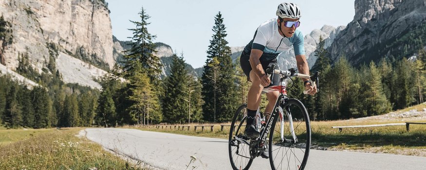 Fahrradfahrer fährt auf Bergstraße mit Felsen und Bäumen im Hintergrund