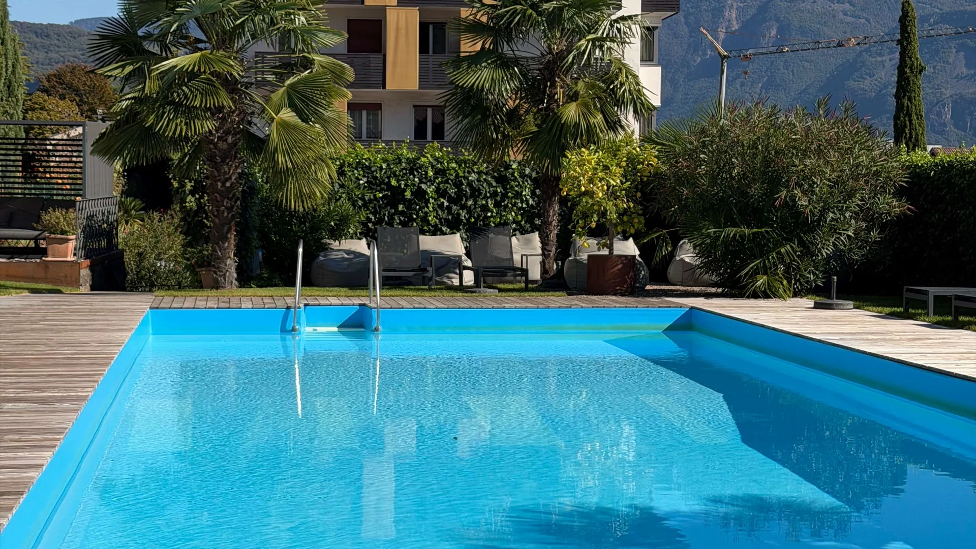 Blue swimming pool in front of modern house with palm trees and mountains