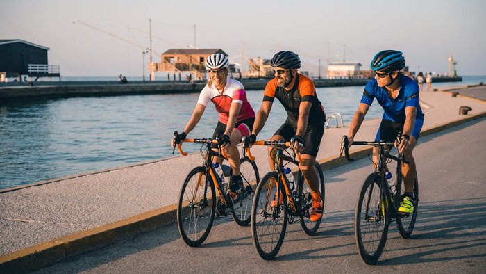 Tre ciclisti con abbigliamento colorato pedalano lungo il lungomare al chiaro cielo