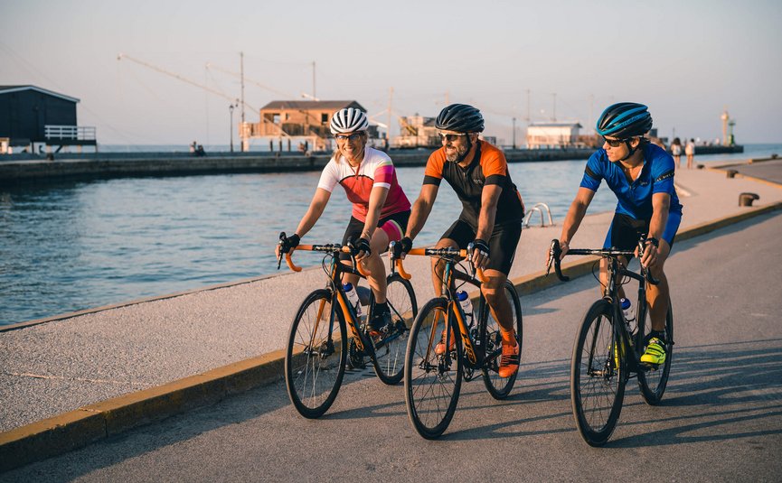 Three cyclists in colorful outfits riding bikes along waterfront on clear day