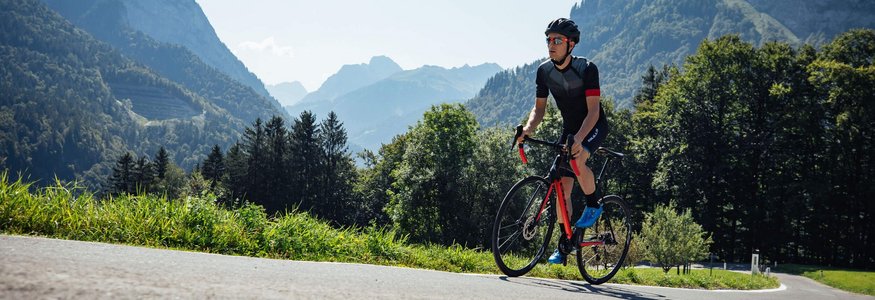 Radfahrer mit Helm fährt auf Bergstraße bei sonnigem Wetter