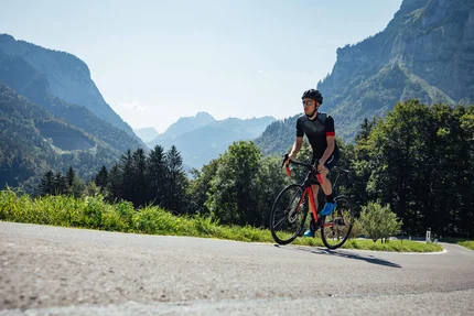Radfahrer mit Helm fährt auf Bergstraße bei sonnigem Wetter