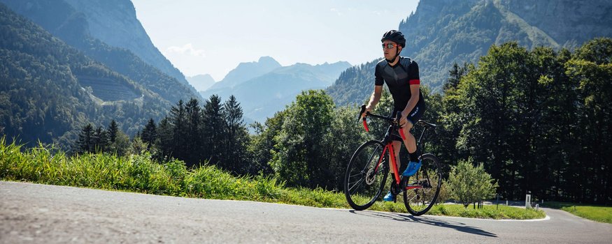 Gämsle Hotel, Wirtshaus & mehr .. © Bregenzerwald Tourismus - Sebastian Stiphout Cyclist wearing helmet rides on mountain road on a sunny day