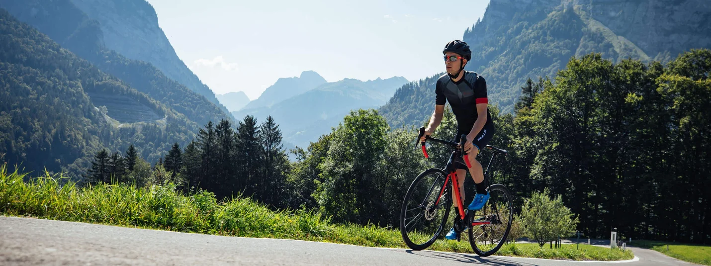 Giro del Furkajoch Bregenzerwald © Bregenzerwald Tourismus - Sebastian Stiphout Ciclista con casco su strada di montagna in una giornata di sole