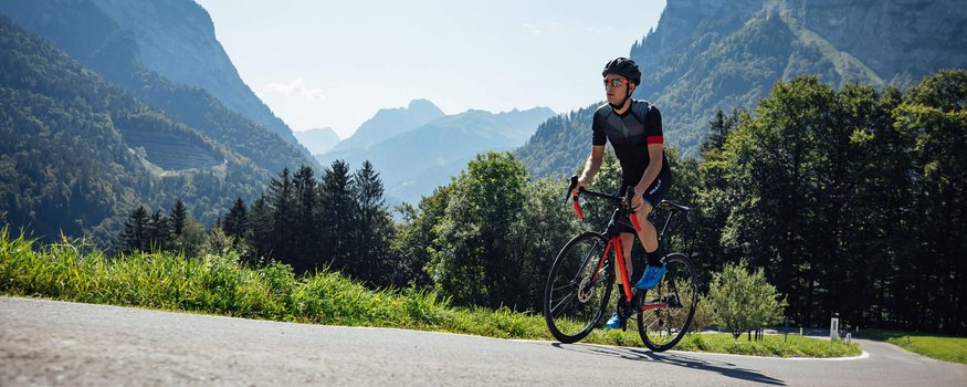 Rennrad Urlaub in Vorarlberg © Bregenzerwald Tourismus - Sebastian Stiphout Radfahrer mit Helm fährt auf Bergstraße bei sonnigem Wetter