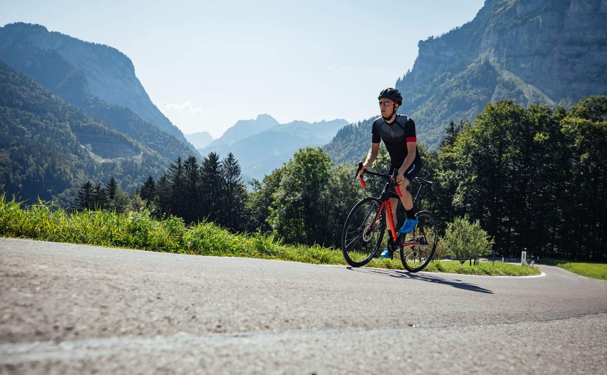 Ciclista con casco su strada di montagna in una giornata di sole