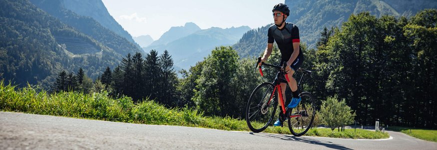Ciclista con casco su strada di montagna in una giornata di sole