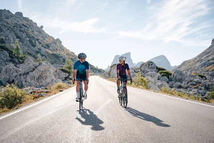 Two cyclists riding on mountain road between rocks under clear sky