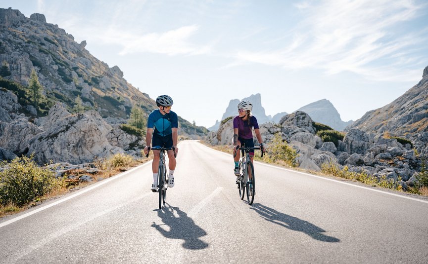 Two cyclists riding on mountain road between rocks under clear sky